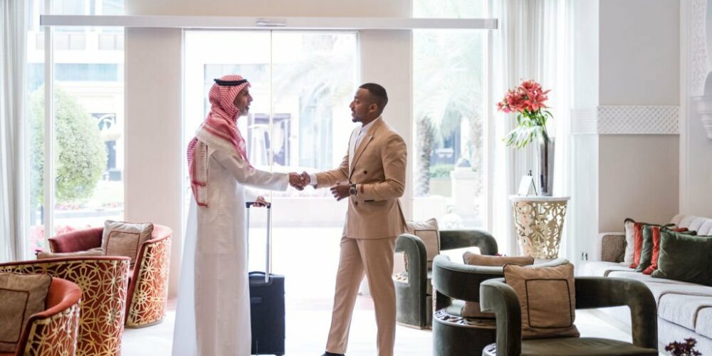 Full length side view of mid adult Black businessman in suit concluding dealings with mature Middle Eastern colleague with luggage.